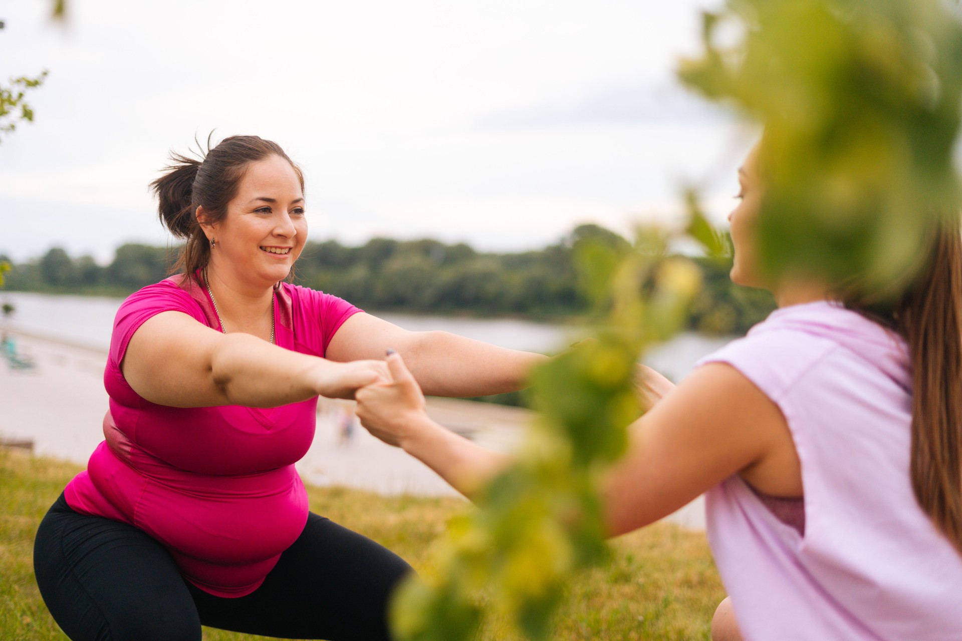 Medium shot of professional fitness female trainer giving personal training to overweight young woman outdoor in summer day.